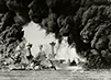 In this black and white photograph, battleships are surrounded by black smoke during the attack on Pearl Harbor.