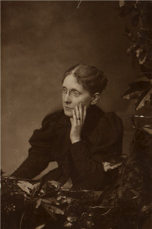 A woman seated with her left hand on her left cheek, and looking to her right.
