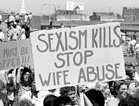 Crowd with signs of 'Rapists must be stopped!,' and 'Sexism Kills Stop Wife Abuse'