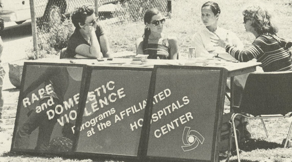Four women sitting at a table with identifying sign.