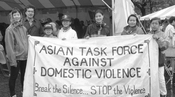 Asian American adults and children stand holding a banner and looking at the viewer.