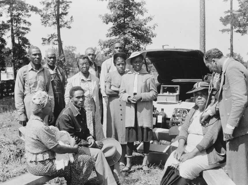 10 African American men and women wait as seated woman receives treatment from a doctor.