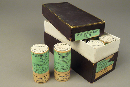 Open box showing tops of small wood canisters inside; two green labeled canisters are next to the box.