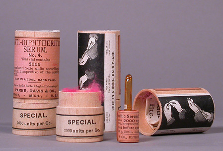 Three pink labeled wood canisters; one canister is open and glass serum ampule is next to it.