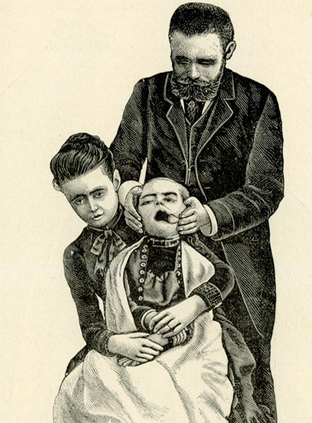 Front view of a seated woman holding a child in her lap; a man stands behind her holding the child’s head; a tool holds the child’s mouth open.