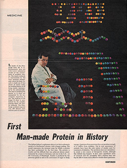 Seated man in a white lab coat with a diagram of the structure of insulin made out of colored spheres superimposed on a black background.