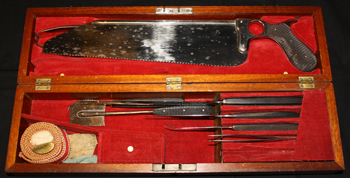 Color photograph of an amputation box holding a variety of metal tools, including a saw.
