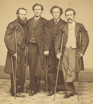 Sepia photograph of four smartly dressed men, each missing a leg and using crutches, standing in a group.