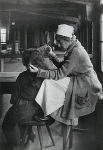 Side view of a uniformed, female, white nurse picking through the long curly hair of a woman.