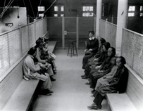Asian women and babies sit on benches in a detention area with one white woman.