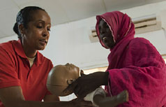 African America woman hands an infant sized mannequin to an African woman.