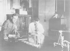 Two men in a Hygienic Laboratory's Division of Pathology and Bacteriology laboratory. The man on the right is looking into a microscope.
