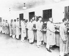 Ambulatory patients wearing striped robes stand in a cafeteria food line at Galveston's Public Health Service Hospital holding trays.