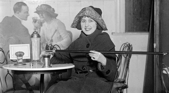 Woman sitting in café pouring alcohol into her glass from a hollowed out cane.