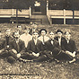 Fifteen White male nurses sitting in a group on a grass lawn.