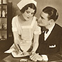 Two White film stars. Female nurse sits on the male doctors' leg to write in a notebook.