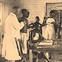 A White male doctor and three African female nurses in white aprons tend to African patients.