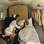 A White female nurse in white holds oxygen up to an elderly White male patient in an airplane.