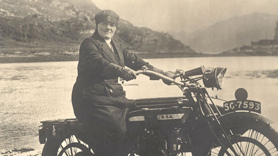 A White female nurse on a motorcycle, looking at the viewer, castle in background.