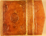 The lower cover and flap of MS A 14 with a central panel stamp of shallow-scalloped ovoid outline with two small pendants. There are also blind-stamped corner panels whose inner field is decorated in the same manner as the central panel, with twisted and tied cloud ribbon forms with vine work studded with flower heads (probably carnations). These deeply-impressed blind stamps are framed by blind-tooled fillets either side of a string of small circles; similar frames decorate the fore-edge flap. The envelope flap is decorated with similar corner panels and frames and one small stamp identical to one of the pendants on the covers.