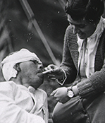 A woman lights a cigarette for a wounded man.