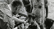 A man examines a child's mouth outdoors.