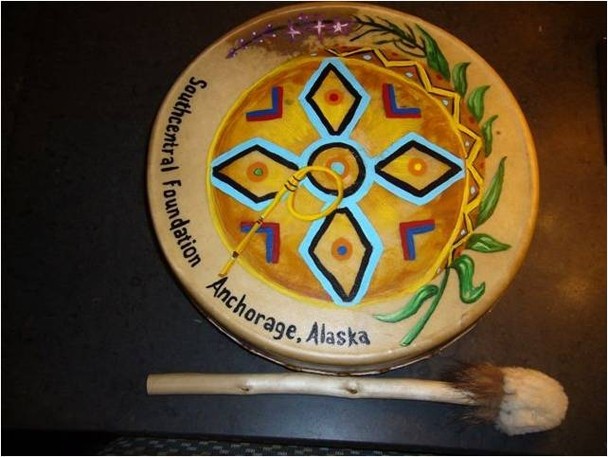 A round, flat, painted drum and a hand-carved drum stick with a large, round tip.