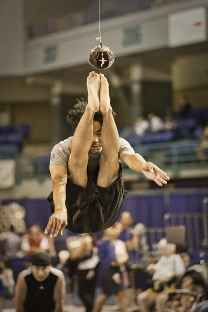 Color image of a male in mid-air performing a high kick. His feet are about to make contact with a suspended ball.