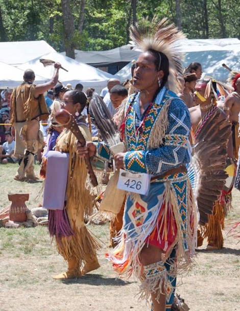 Color photograph of a Native American male dancing in traditional attire adorned with eagle feathers and intricate designs.