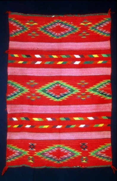 Color image of a handmade, bright red rug, with various embroidered designs.