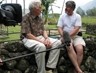 Color image of two men talking during an interview while sitting on a waist-high wall made of rocks.