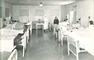 Black and white photograph of several patients lying in their beds inside of a hospital ward.