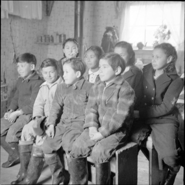 Black and white photograph of eight Unangan children sitting on two benches.