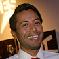 Latino man smiling holding several pieces of paper.