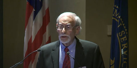 An older white man speaks at a podium.