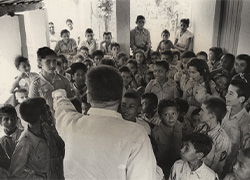 A large group of uniformed children are gathered around a health educator at a youth health club.