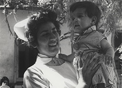 Outside, a woman in nurse’s uniform smiles while holding a child standing on her left palm.