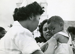 A woman holds a child getting a shot on the upper left arm.