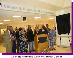 Group of people standing underneath a banner in a hospital ward.  Courtesy Alameda County Medical Center