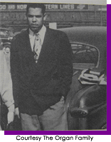 Man in jacket and tie standing in front of a car with a stack of books resting on the car. Courtesy The Organ Family