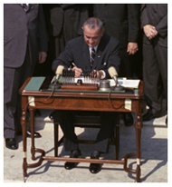 President Lyndon B. Johnson signs the Economic Opportunity Act in the White House Rose Garden as crowd looks on