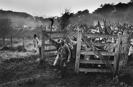 Members of the Landless Workers' Movement march through gates holding tools and flags