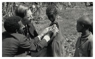 Dr. D.A. Henderson and colleague adminster a smallpox vaccination to a child as other children observe