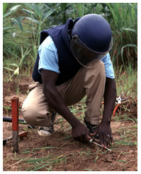 Deminer wearing saftey gear removes a landmine from the ground