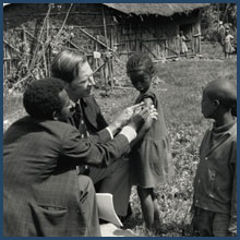 Dr. D. A. Henderson and colleague administer a smallpox vaccination to a child as other children observe