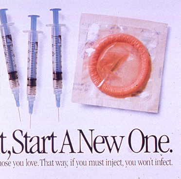 Color photograph of a line of syringes with a condom on the far right
