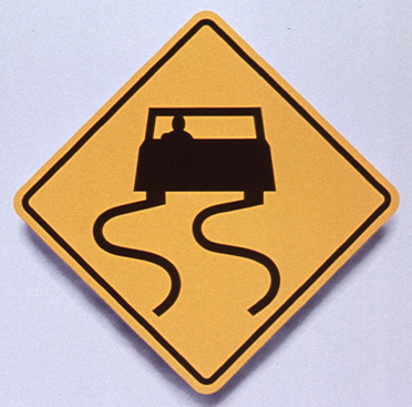 Yellow square road sign that has black outline of car with curved lines behind it indicating curves in the roadway ahead above text