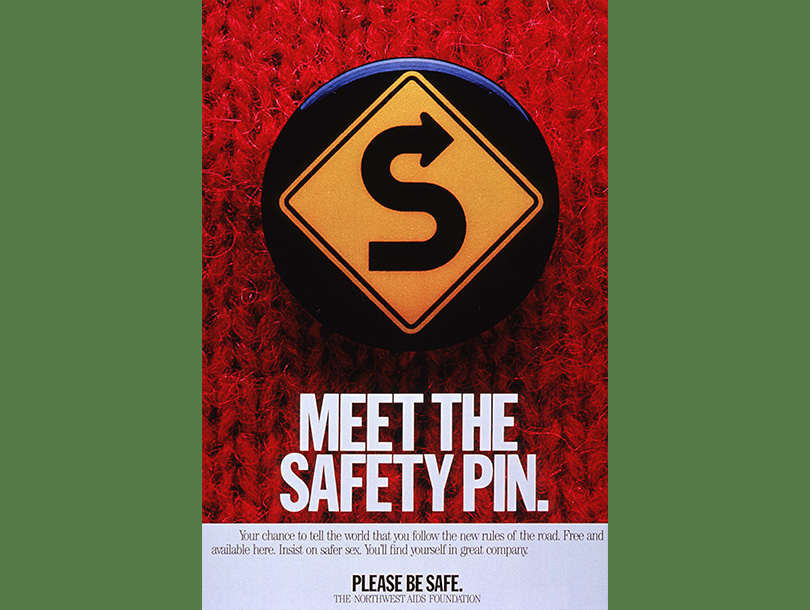 Color photograph of a safety pin on a red sweater; the pin has a yellow roadside on it