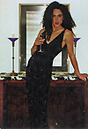 A woman in a long black evening gown holds a wine flute in her right hand while leaning against a table with her left hand.