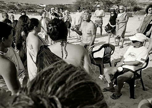 Black and white photograph of people, some wearing traditional Native Hawaiian garb, standing in a loose circle.